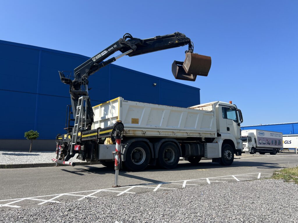 MAN wywrotka z żurawiem HIAB X-HIPRO 192 unoszącym chwytak przy hali